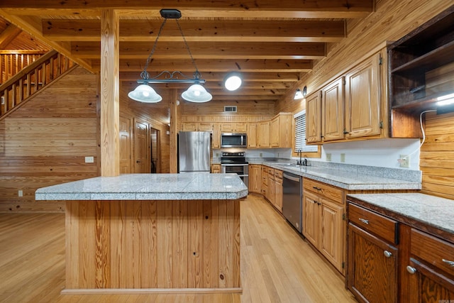 kitchen featuring a kitchen island, beam ceiling, a sink, appliances with stainless steel finishes, and light wood-type flooring