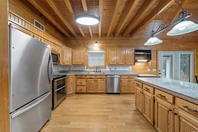 kitchen featuring light wood finished floors, visible vents, wooden walls, appliances with stainless steel finishes, and a sink