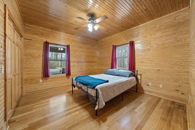 bedroom with wooden walls, light wood-style flooring, wooden ceiling, and a ceiling fan