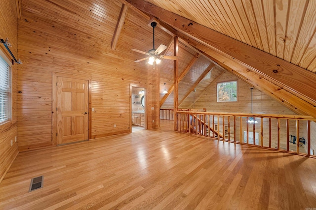 additional living space with visible vents, beamed ceiling, wood walls, wood ceiling, and wood finished floors