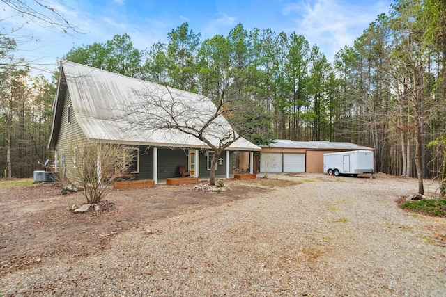 view of front of property featuring cooling unit, driveway, a porch, a garage, and metal roof