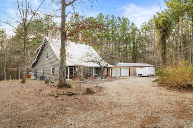 view of front facade featuring central AC, dirt driveway, an outdoor structure, an attached garage, and metal roof