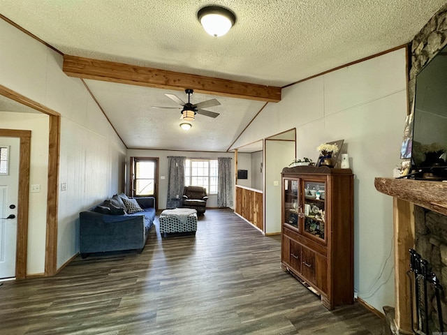 living area featuring a ceiling fan, dark wood finished floors, lofted ceiling with beams, a fireplace, and a textured ceiling