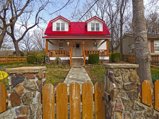 dutch colonial featuring a porch, a fenced front yard, and metal roof