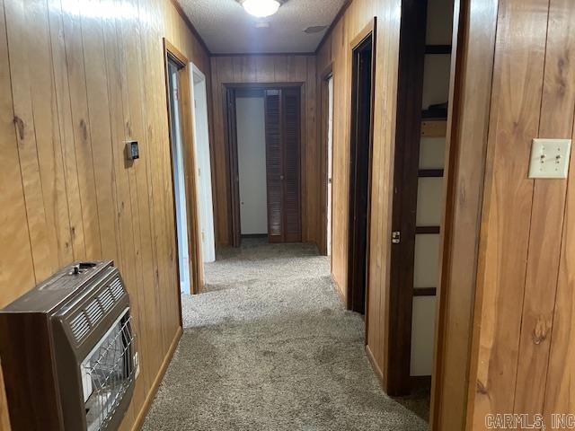 hall featuring carpet flooring, wooden walls, heating unit, and a textured ceiling