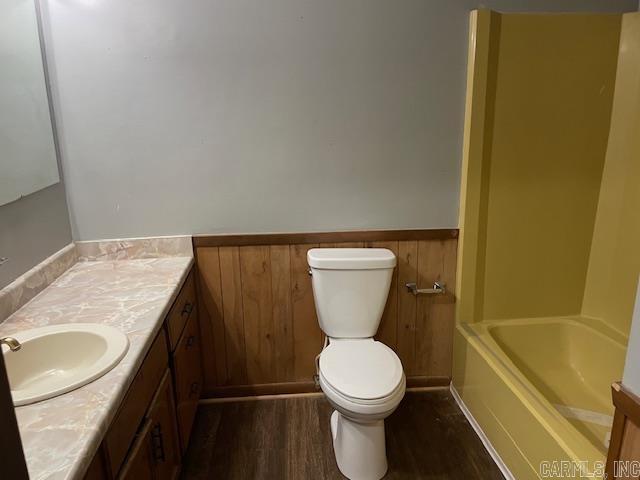 full bathroom featuring toilet, a tub to relax in, wood finished floors, wainscoting, and vanity