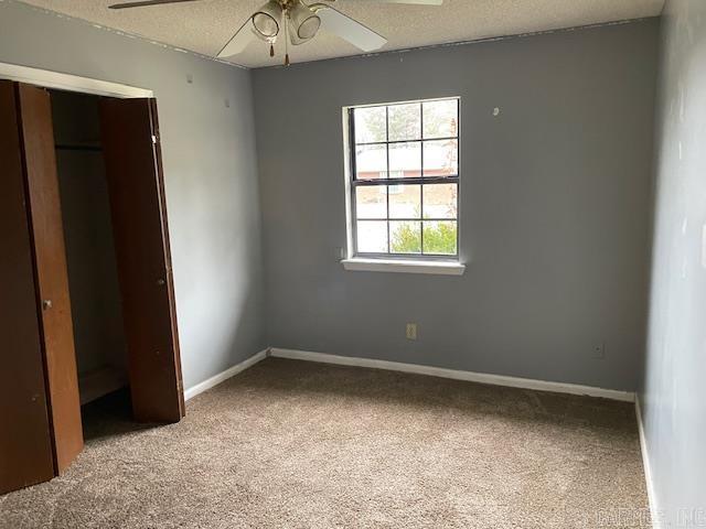 unfurnished bedroom with a closet, light colored carpet, a textured ceiling, and baseboards