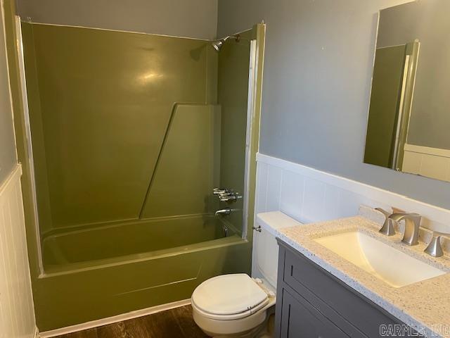 full bath featuring a wainscoted wall, toilet, wood finished floors, vanity, and  shower combination