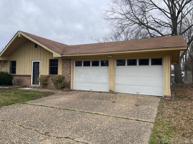 ranch-style home with board and batten siding, a garage, brick siding, and driveway