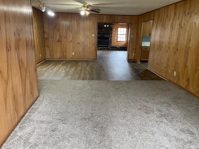 carpeted empty room with wooden walls, a stone fireplace, and ceiling fan