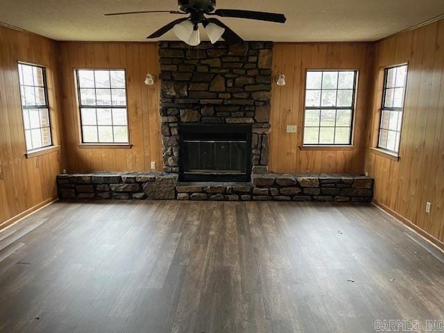 unfurnished living room with wood walls, a fireplace, a ceiling fan, and wood finished floors