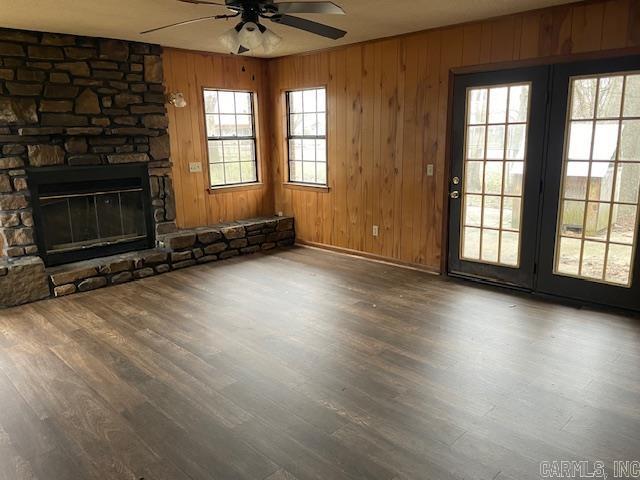 unfurnished living room featuring wood finished floors, wooden walls, a fireplace, and ceiling fan