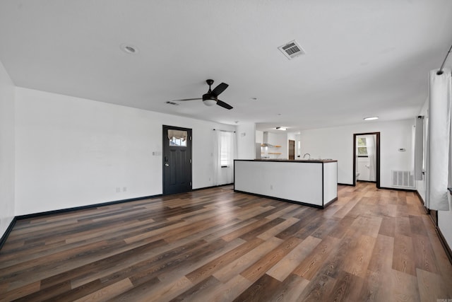 unfurnished living room with ceiling fan, visible vents, baseboards, and wood finished floors