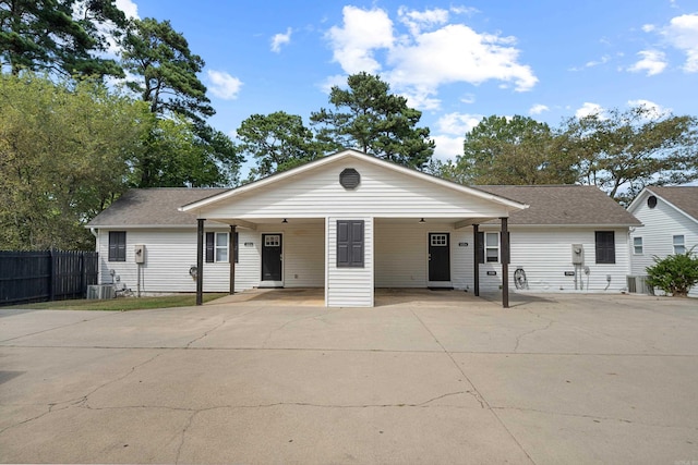 ranch-style home featuring an attached carport, fence, roof with shingles, central AC, and driveway