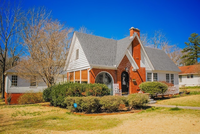 view of front of home featuring a front lawn, brick siding, a chimney, and a shingled roof