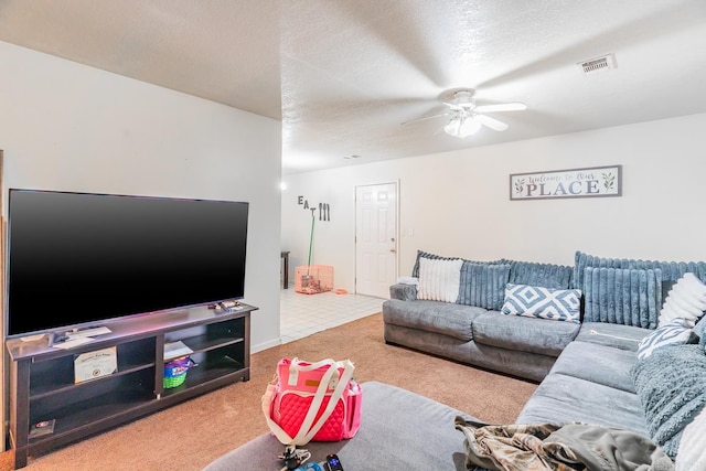 carpeted living area with tile patterned floors, visible vents, a textured ceiling, and a ceiling fan