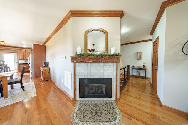 living room with light wood-type flooring, visible vents, ornamental molding, a tiled fireplace, and baseboards