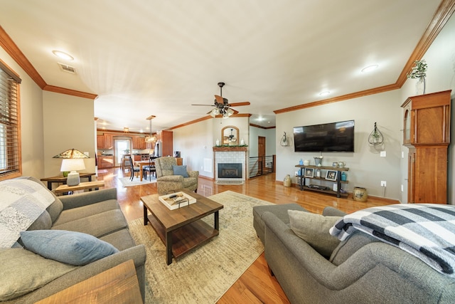 living area featuring a ceiling fan, visible vents, light wood finished floors, a tile fireplace, and crown molding