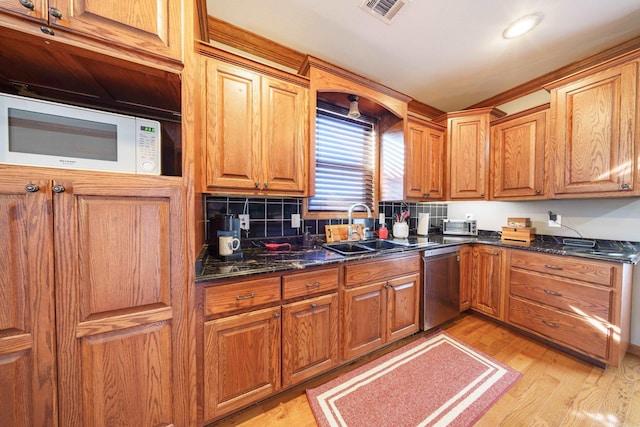 kitchen with white microwave, dishwasher, brown cabinetry, and a sink