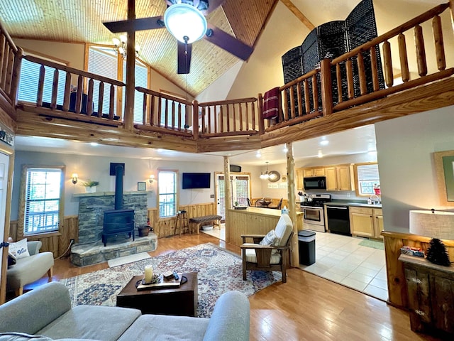 living area with plenty of natural light, wainscoting, a wood stove, and light wood-style floors