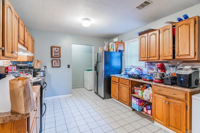 kitchen with visible vents, under cabinet range hood, light countertops, freestanding refrigerator, and washer / clothes dryer