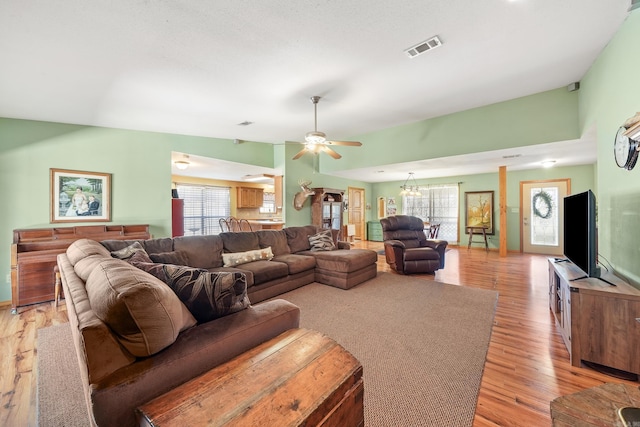 living area featuring ceiling fan with notable chandelier, a healthy amount of sunlight, visible vents, and light wood-type flooring