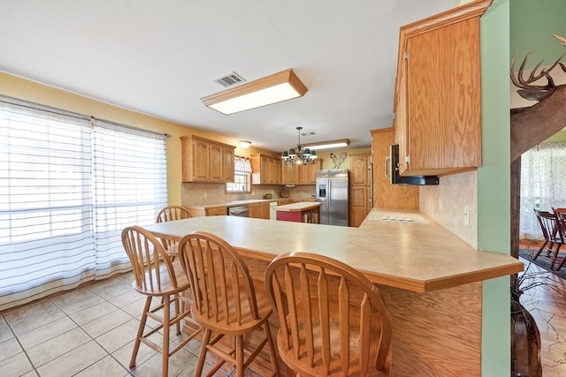 kitchen featuring a kitchen bar, light countertops, appliances with stainless steel finishes, a peninsula, and a notable chandelier