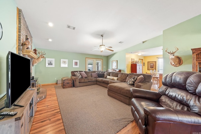 living room with visible vents, lofted ceiling, a wood stove, and light wood finished floors