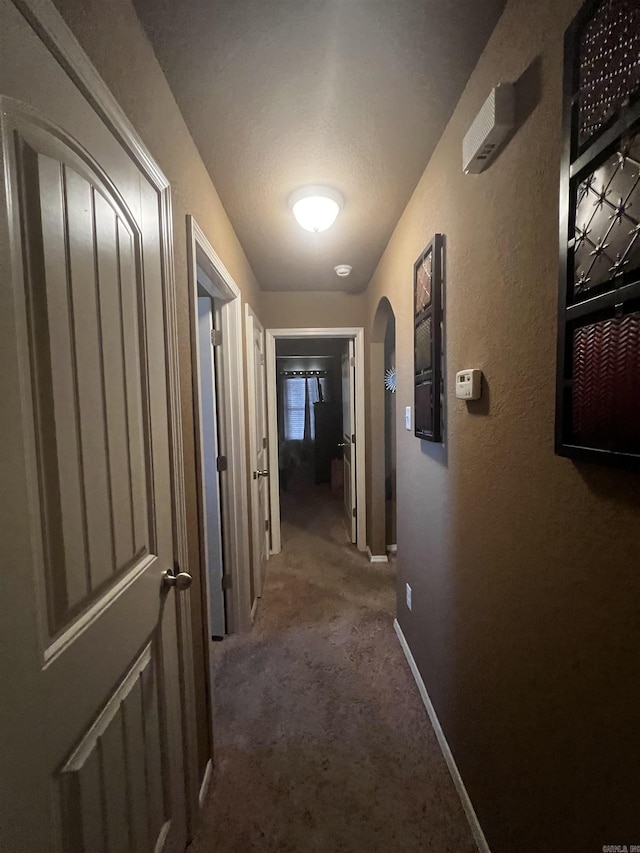 hallway with baseboards, arched walkways, carpet, and a textured wall