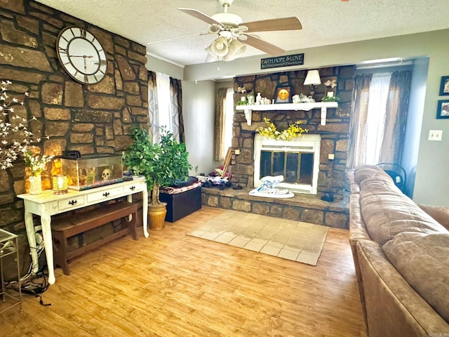 living area with a fireplace, ceiling fan, wood finished floors, and a textured ceiling