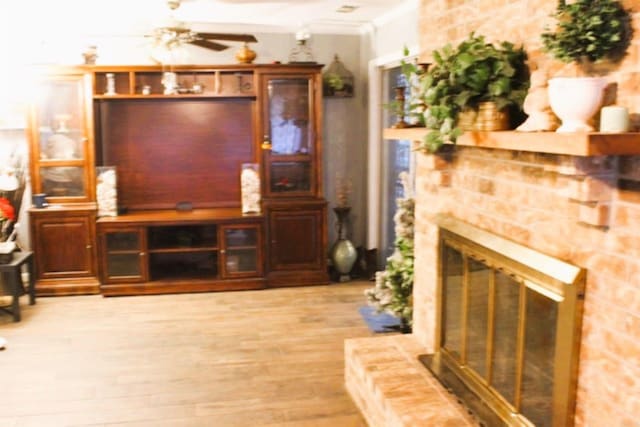 living room featuring a ceiling fan, a fireplace, light wood finished floors, and ornamental molding