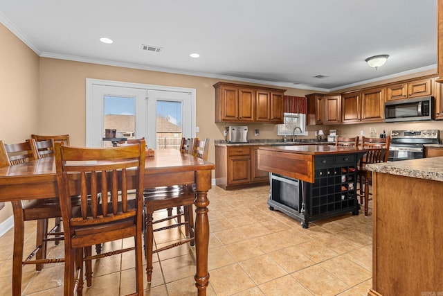 kitchen with crown molding, light tile patterned floors, brown cabinets, stainless steel appliances, and a sink