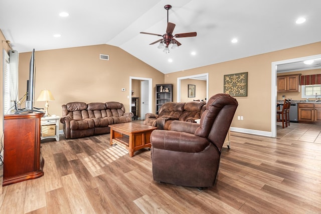 living room with visible vents, baseboards, light wood-style floors, and vaulted ceiling