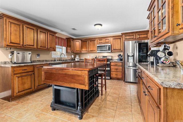 kitchen featuring butcher block countertops, ornamental molding, light tile patterned floors, brown cabinets, and appliances with stainless steel finishes