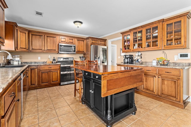 kitchen featuring light tile patterned floors, a sink, stainless steel appliances, crown molding, and brown cabinets