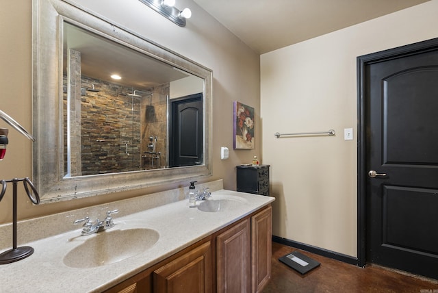 full bathroom with a tile shower, double vanity, baseboards, and a sink