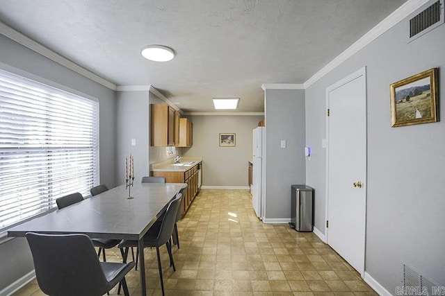 interior space featuring visible vents, brown cabinets, a sink, crown molding, and baseboards