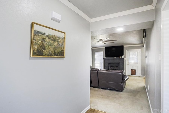 carpeted living room with a ceiling fan, crown molding, a fireplace, and baseboards