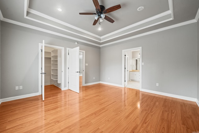 unfurnished bedroom featuring a raised ceiling, crown molding, a spacious closet, and light wood finished floors