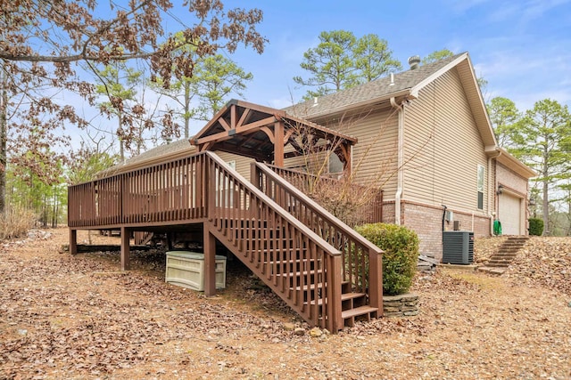 rear view of property with a deck, stairway, roof with shingles, brick siding, and central AC unit