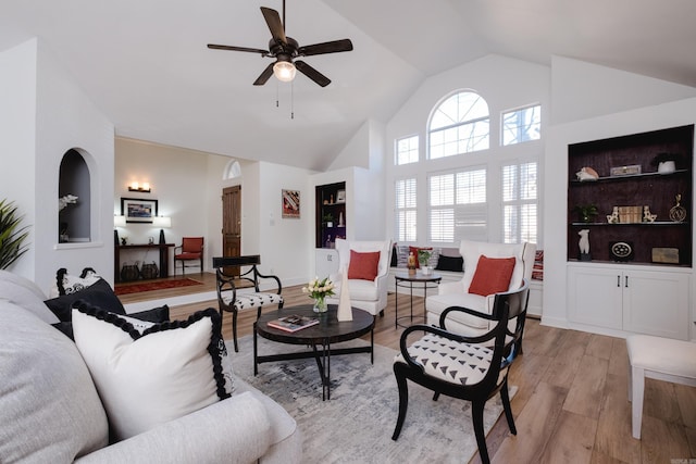 living area featuring built in shelves, baseboards, ceiling fan, light wood-style flooring, and high vaulted ceiling