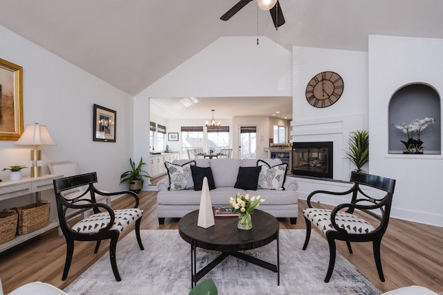 living area with a glass covered fireplace, ceiling fan with notable chandelier, light wood-type flooring, and baseboards