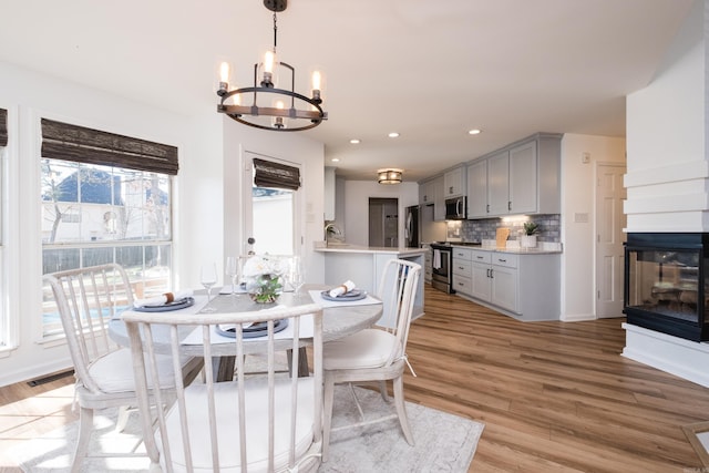 dining room with visible vents, a chandelier, a multi sided fireplace, light wood-style flooring, and recessed lighting