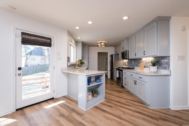 kitchen with a sink, backsplash, appliances with stainless steel finishes, a peninsula, and light wood finished floors