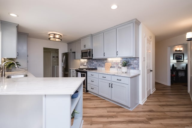 kitchen featuring light wood-style flooring, a sink, stainless steel appliances, decorative backsplash, and light stone countertops