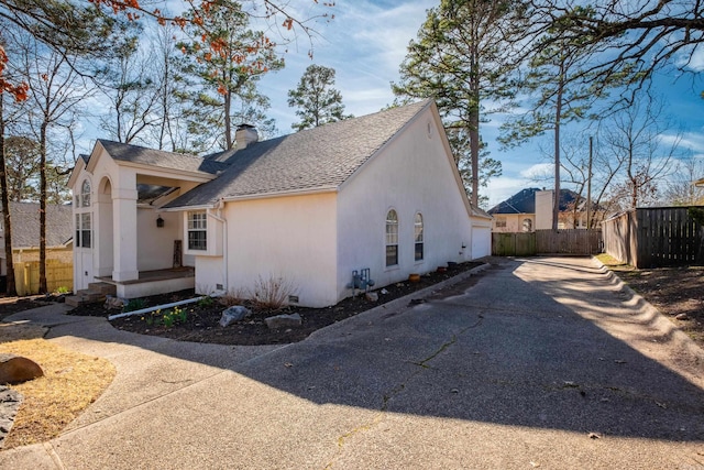 view of side of property featuring stucco siding, fence, a shingled roof, crawl space, and a chimney