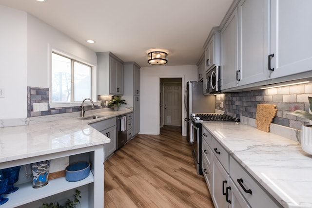 kitchen featuring light stone counters, gray cabinets, a sink, stainless steel appliances, and light wood-type flooring