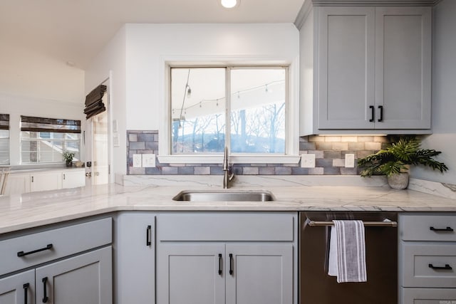 kitchen featuring light stone countertops, dishwasher, decorative backsplash, gray cabinets, and a sink