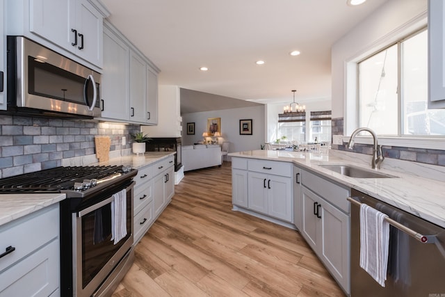 kitchen with a sink, decorative backsplash, light wood-style floors, appliances with stainless steel finishes, and open floor plan