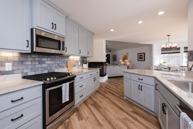 kitchen with open floor plan, light wood-style floors, appliances with stainless steel finishes, a notable chandelier, and tasteful backsplash